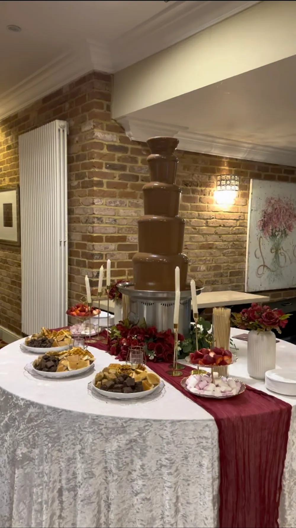 Chocolate fountain with a red runner, flowers and a selection of dipping treats